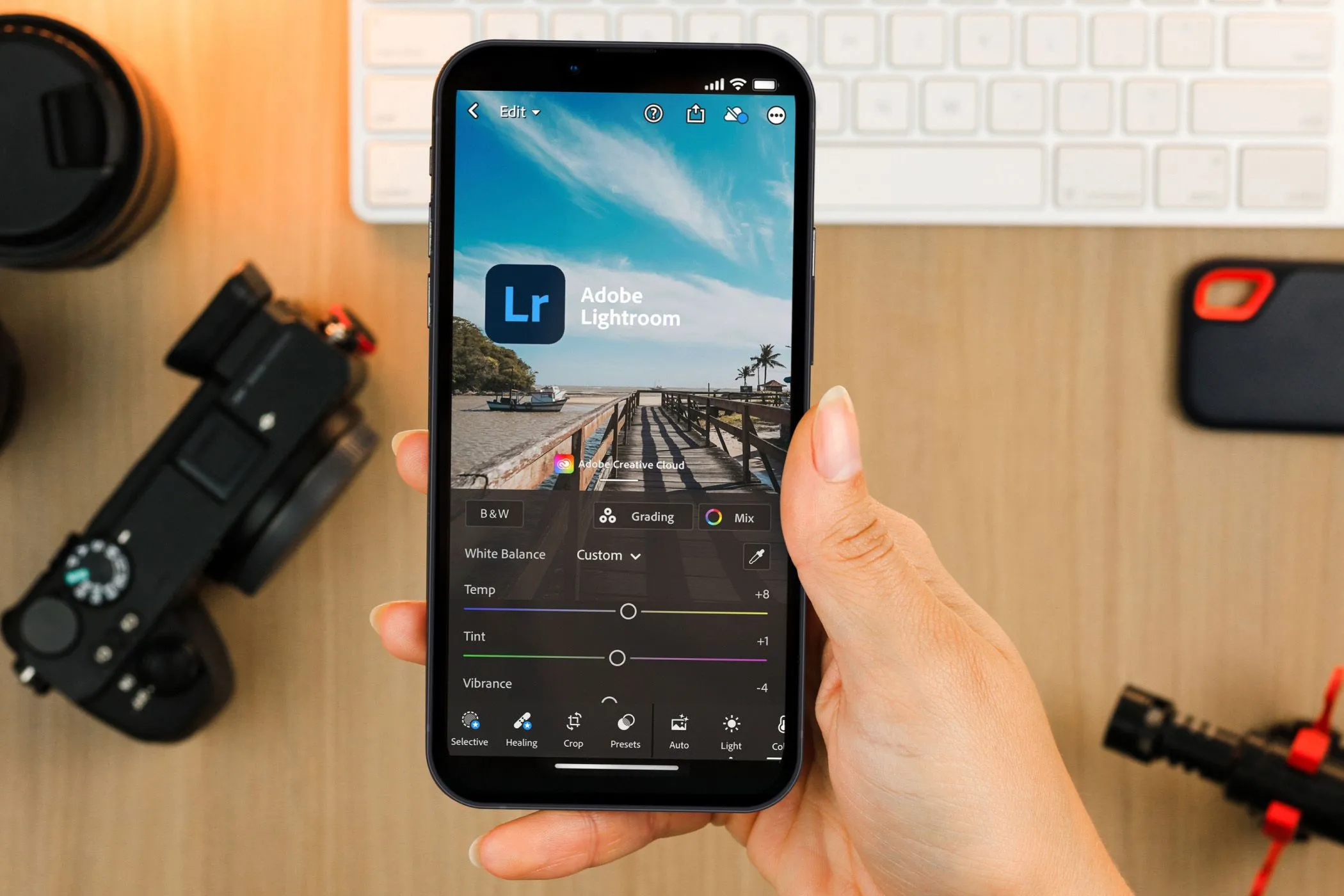 Bàn tay đang cầm điện thoại hiển thị ứng dụng Lightroom Mobile, thể hiện khả năng chỉnh sửa ảnh chuyên nghiệp mọi lúc mọi nơi