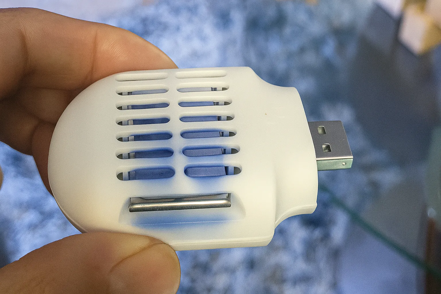 Bàn tay đang cầm một thiết bị đuổi muỗi nhỏ gọn màu trắng chạy bằng cổng USB, tiện lợi cho xe hơi.