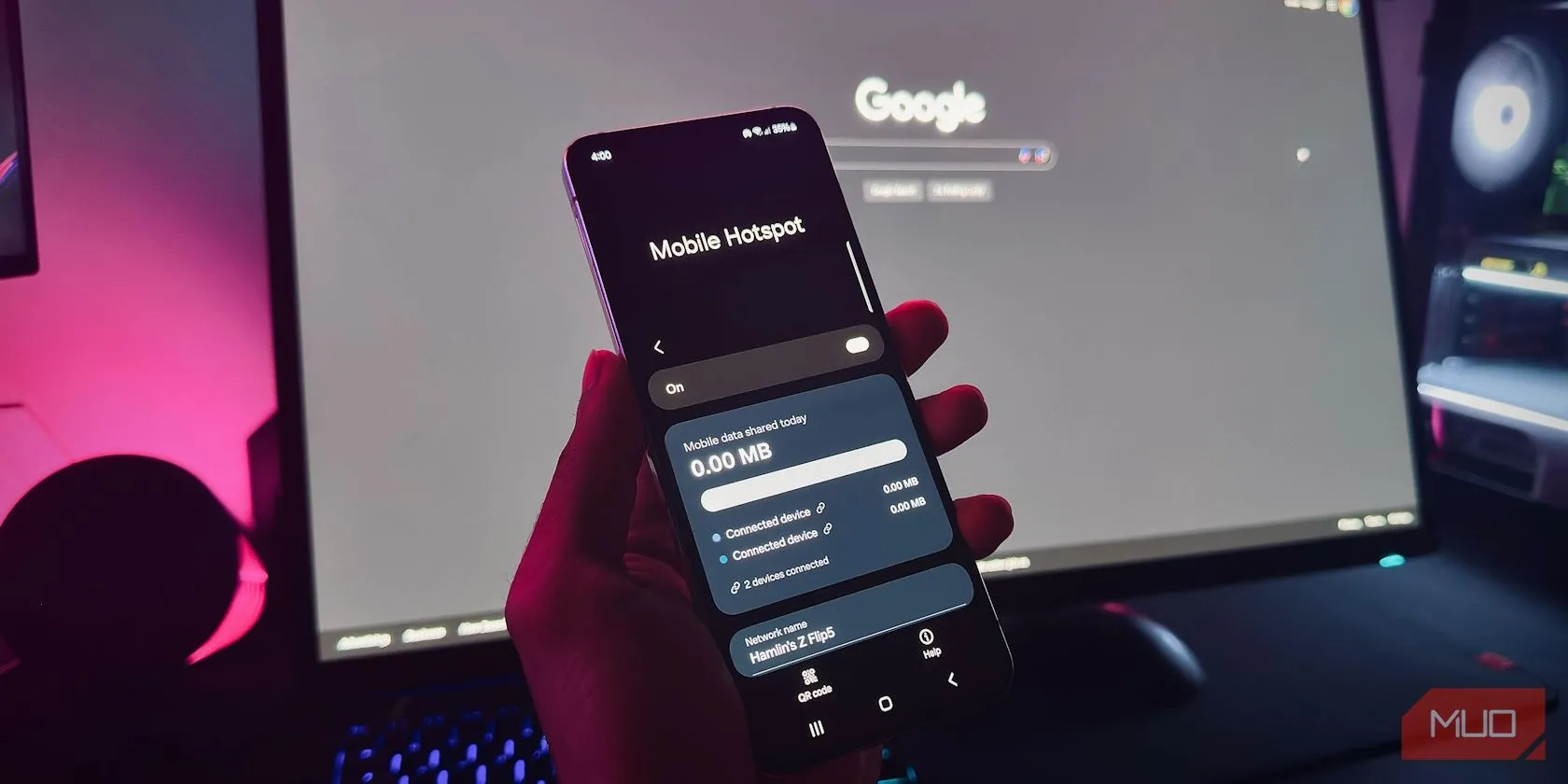 Bàn tay giữ điện thoại Android hiển thị tính năng Điểm phát sóng di động trước màn hình máy tính
