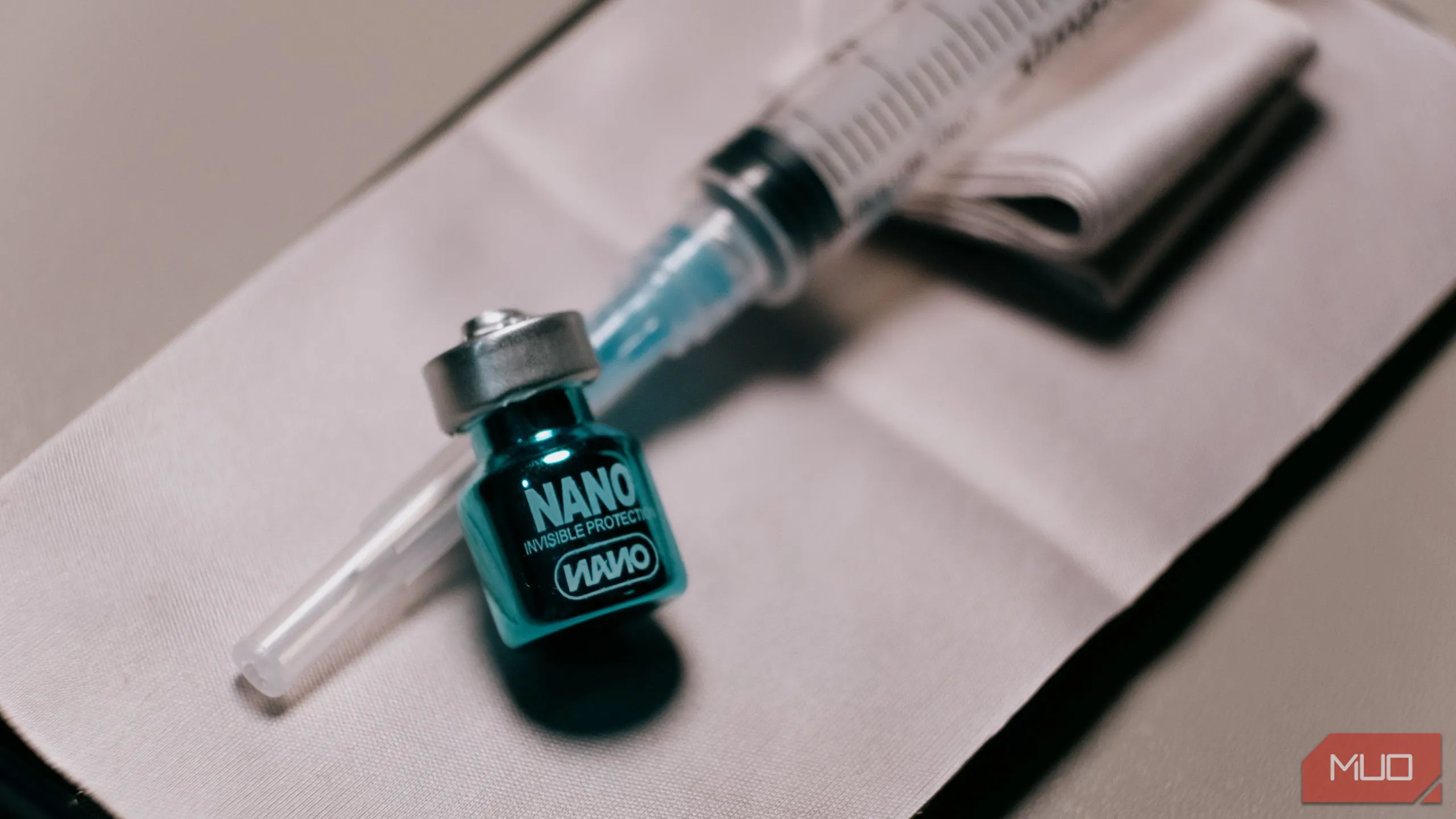 Chai dung dịch phủ Nano Oleophobic bên cạnh ống tiêm, minh họa vật liệu dùng trong thử nghiệm phủ chống bám vân tay cho màn hình điện thoại.