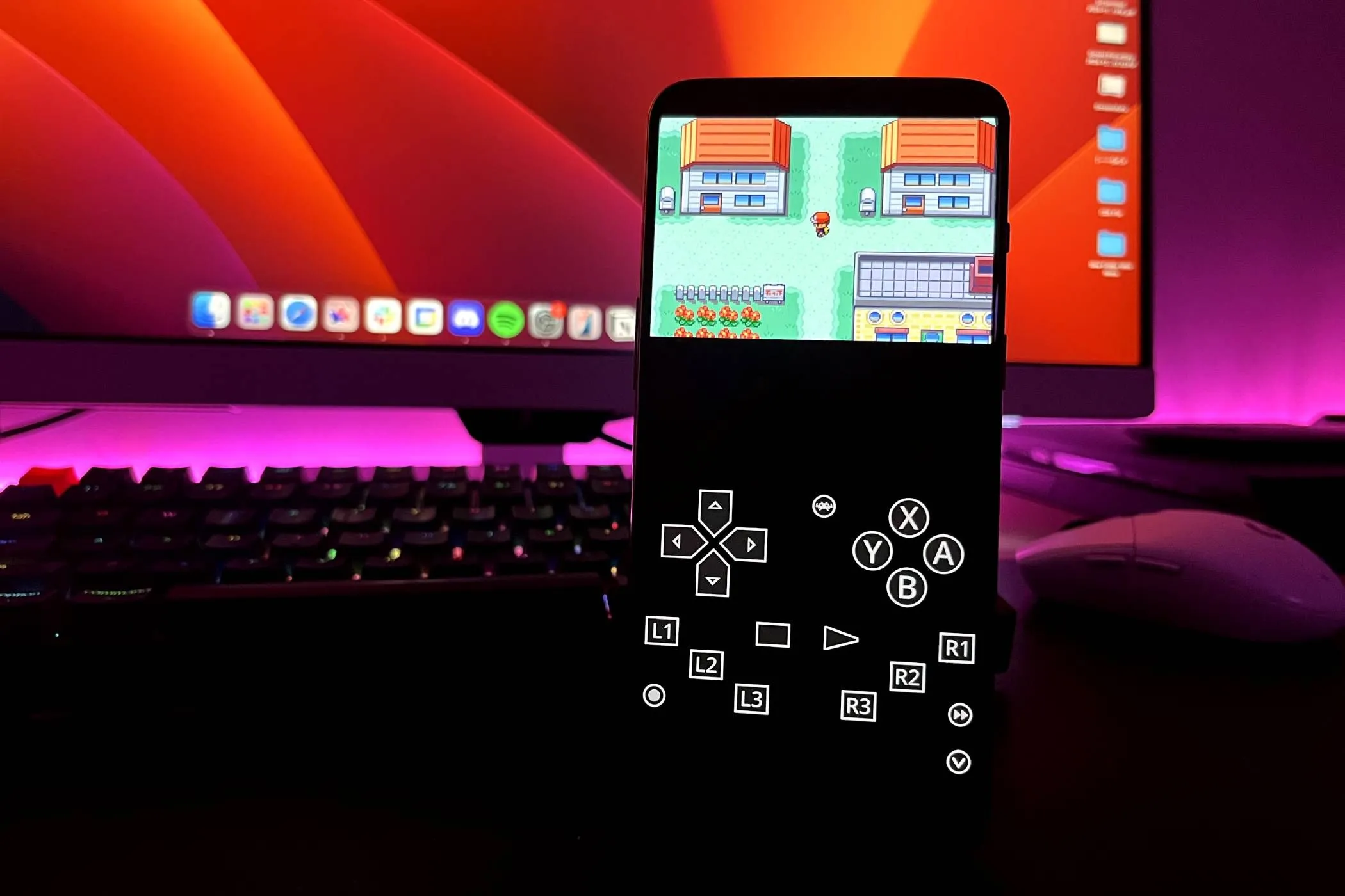 Điện thoại Android đang chạy game Pokémon: Fire Red trên ứng dụng RetroArch, cùng với bàn phím, chuột và màn hình ở phía sau