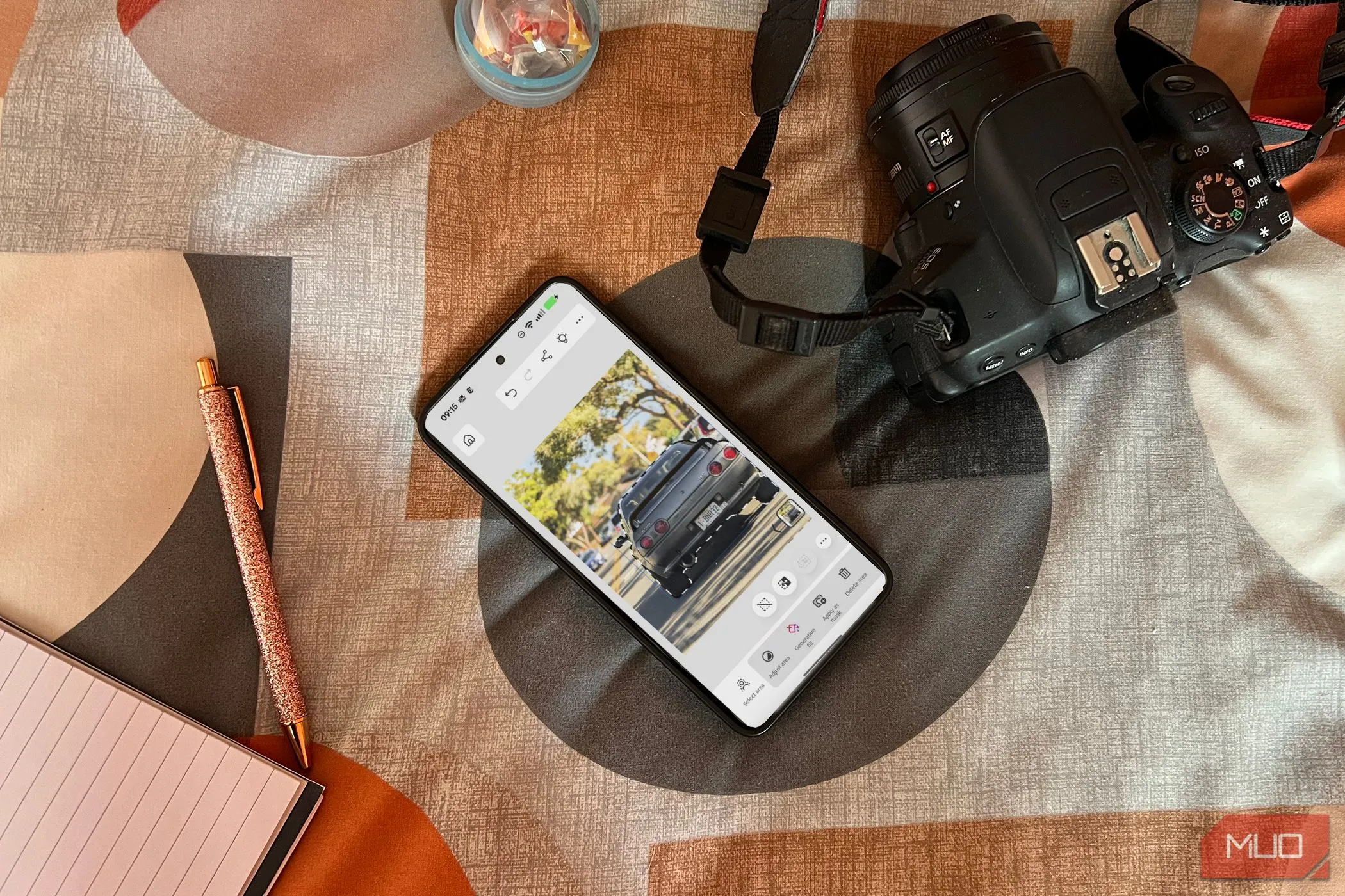 Điện thoại Android hiển thị ứng dụng Photoshop Mobile trên giường, cạnh máy ảnh và sổ ghi chép, thể hiện khả năng làm việc di động.
