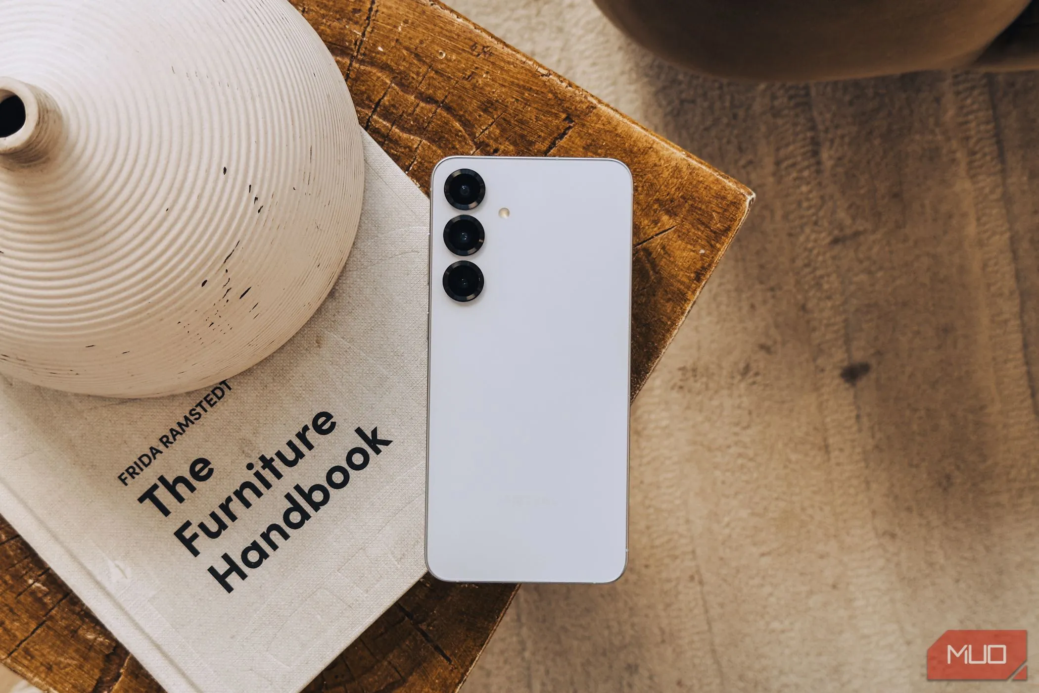Điện thoại Samsung Galaxy S25 màu bạc đặt trên cuốn sách trắng, thể hiện thiết kế và cụm camera sau.