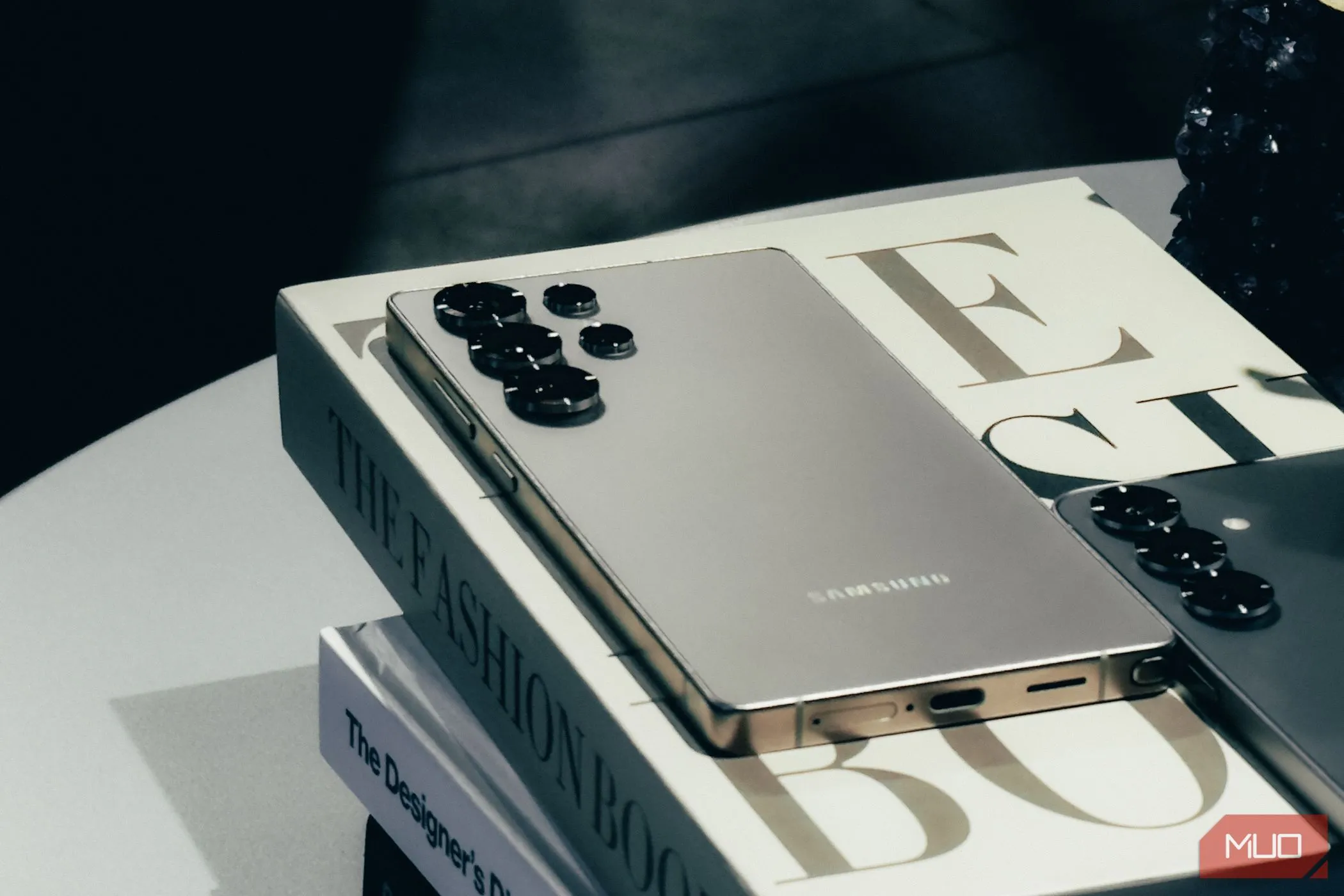 Điện thoại Samsung Galaxy S25 màu Silver Shadow đặt nghiêng trên một cuốn sách, cho thấy chi tiết cạnh bo tròn và màu sắc mới.