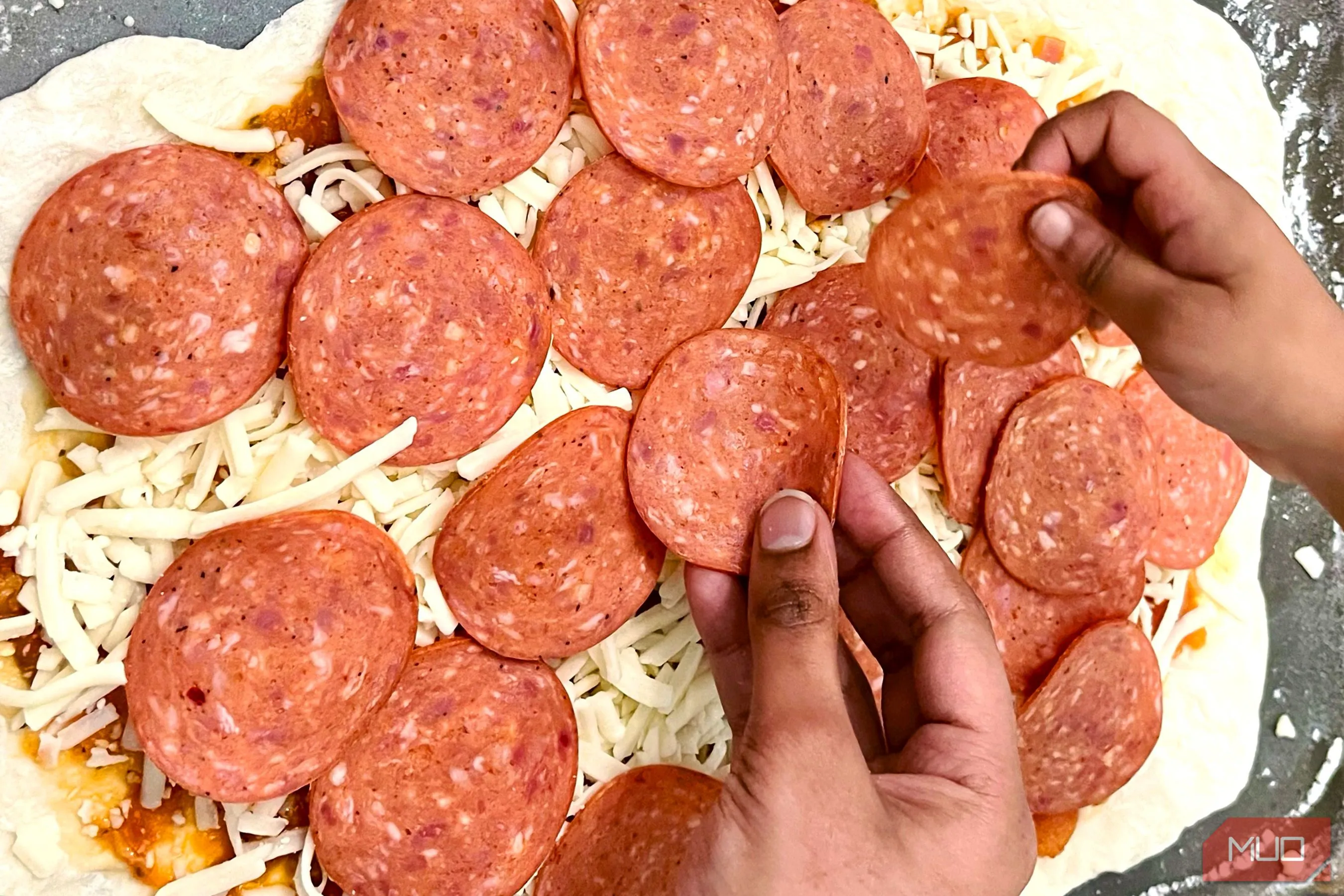 Đôi bàn tay đang rải topping phô mai lên bánh pizza