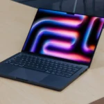 Hình ảnh MacBook Pro sử dụng chip M4 với màn hình nghiêng trên bàn gỗ, tượng trưng cho thế hệ Mac Apple Silicon mới được hỗ trợ bởi macOS 26.