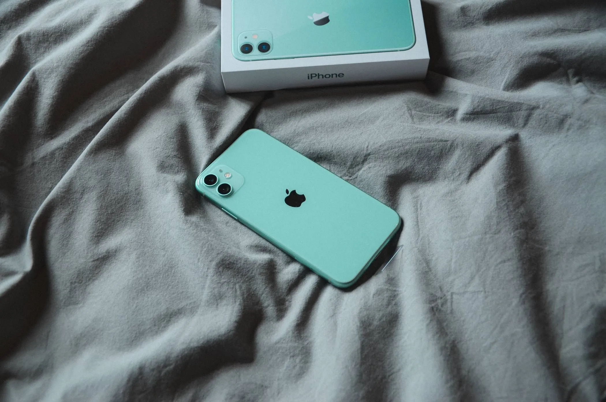 iPhone 11 màu xanh bạc hà đặt trên ga trải giường trắng thể hiện độ bền và thiết kế cao cấp