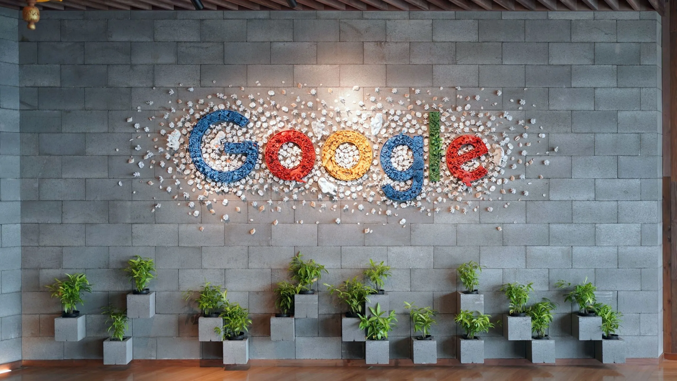Logo Google trên bức tường văn phòng với cây xanh, tượng trưng cho sự đồng bộ hóa liền mạch của Chromebook với hệ sinh thái Google