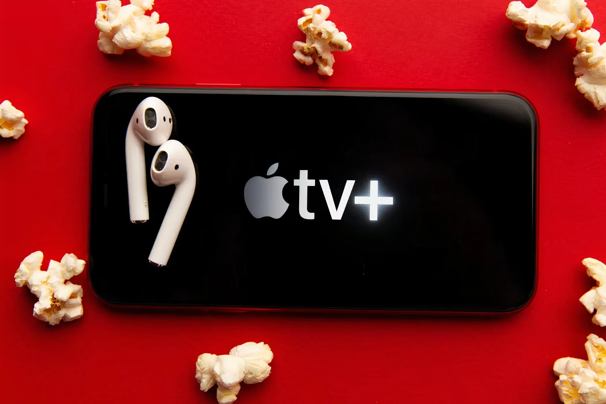 Màn hình điện thoại hiển thị logo Apple TV+, cạnh bên là bỏng ngô và tai nghe, gợi ý trải nghiệm giải trí di động.