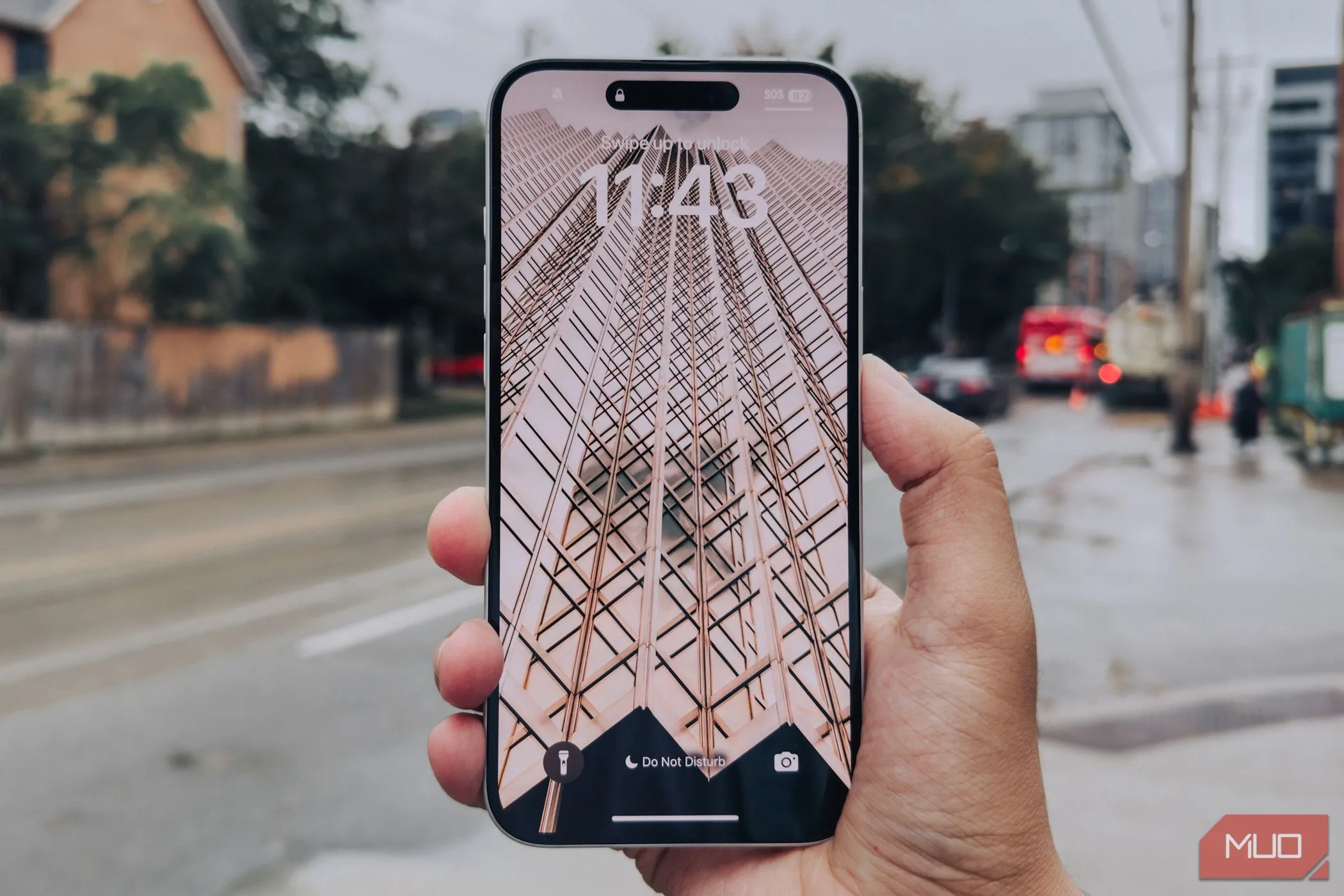 Màn hình iPhone 16 Plus từ cạnh bên trong tay với hậu cảnh thành phố.
