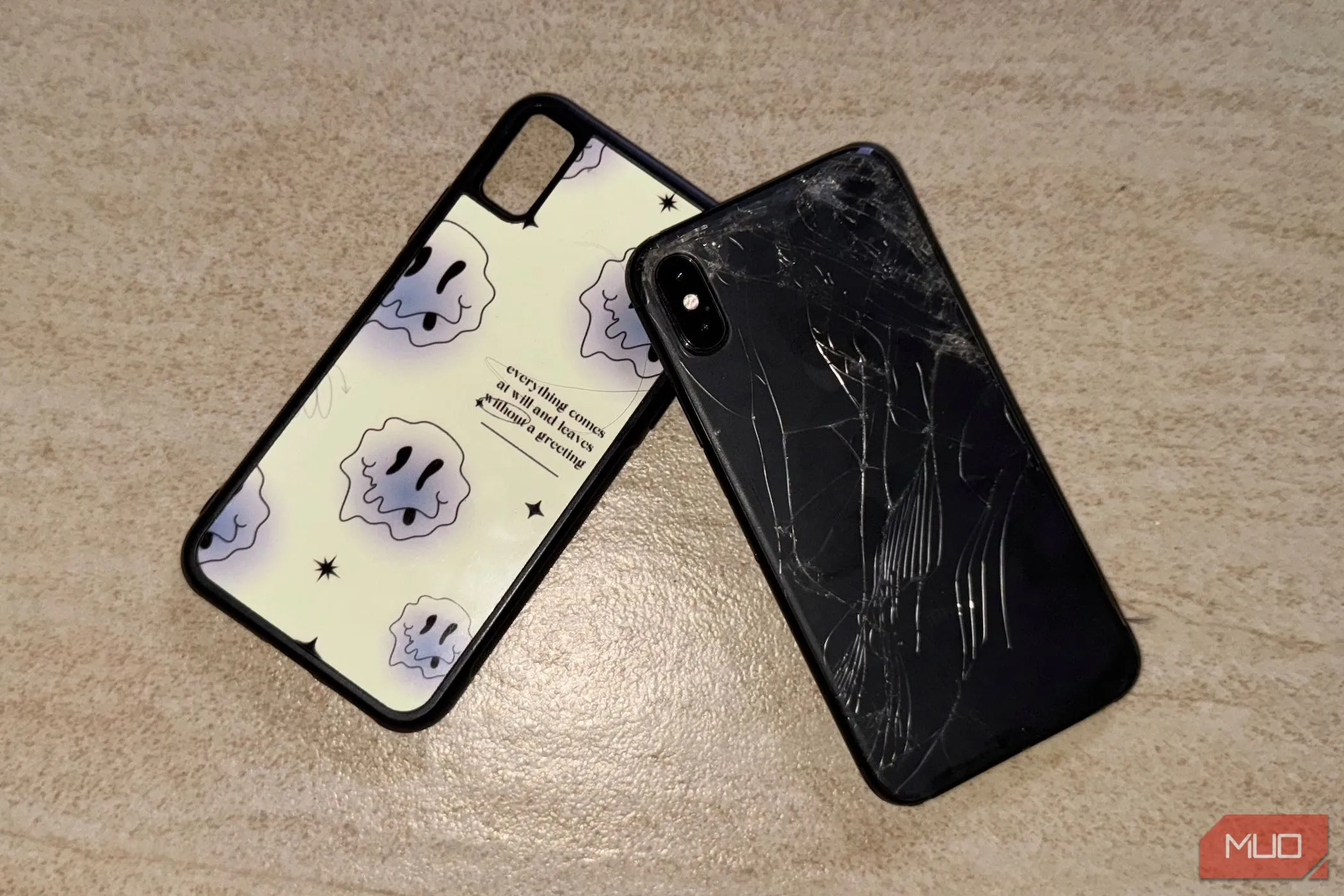 Một chiếc iPhone X với mặt lưng kính bị nứt nằm trên sàn, có ốp lưng.