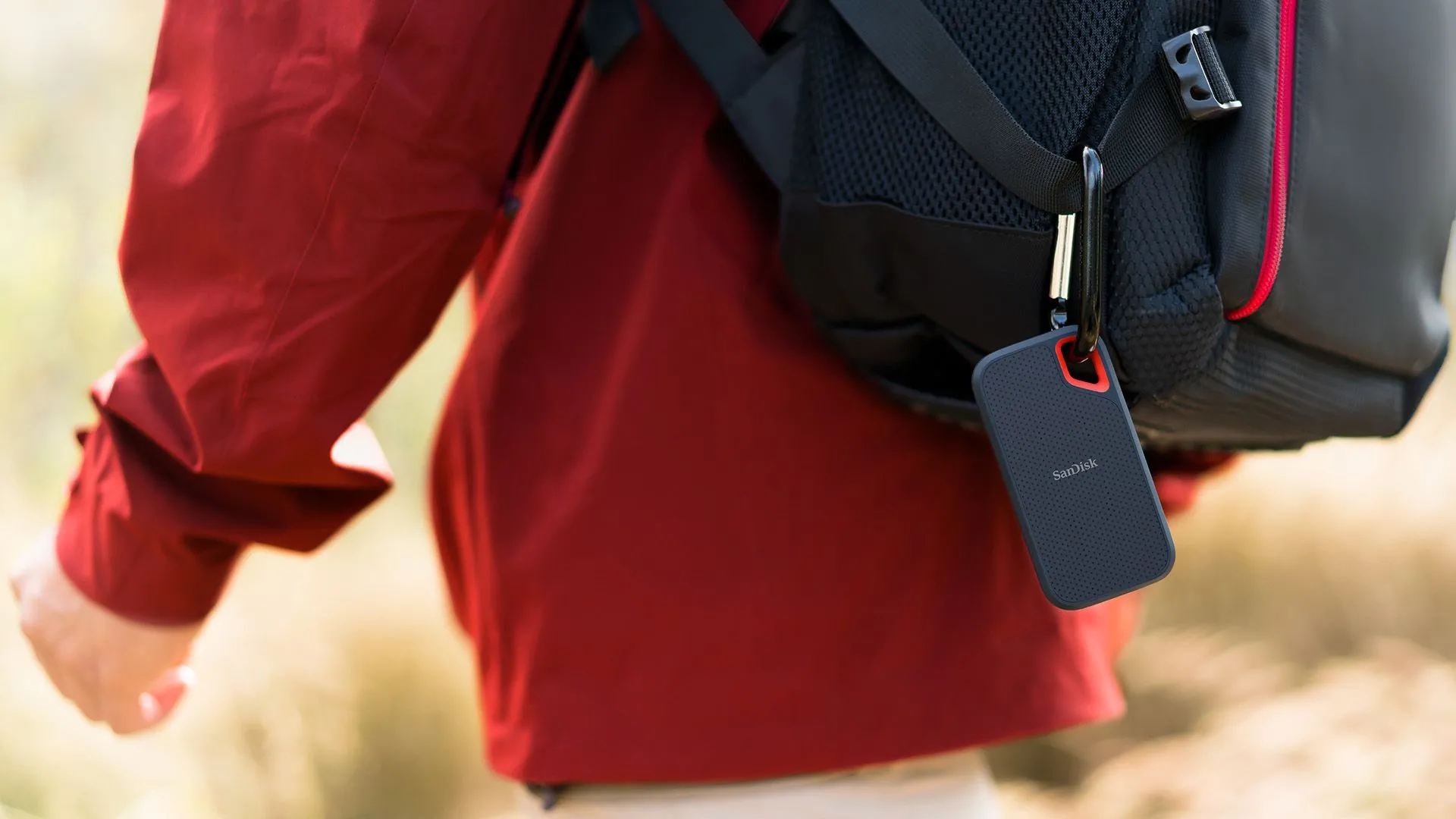 Một người đàn ông đang đạp xe, đeo ba lô và có một chiếc SSD SanDisk Extreme màu đen treo bên ngoài, thể hiện tính di động và bền bỉ khi di chuyển.