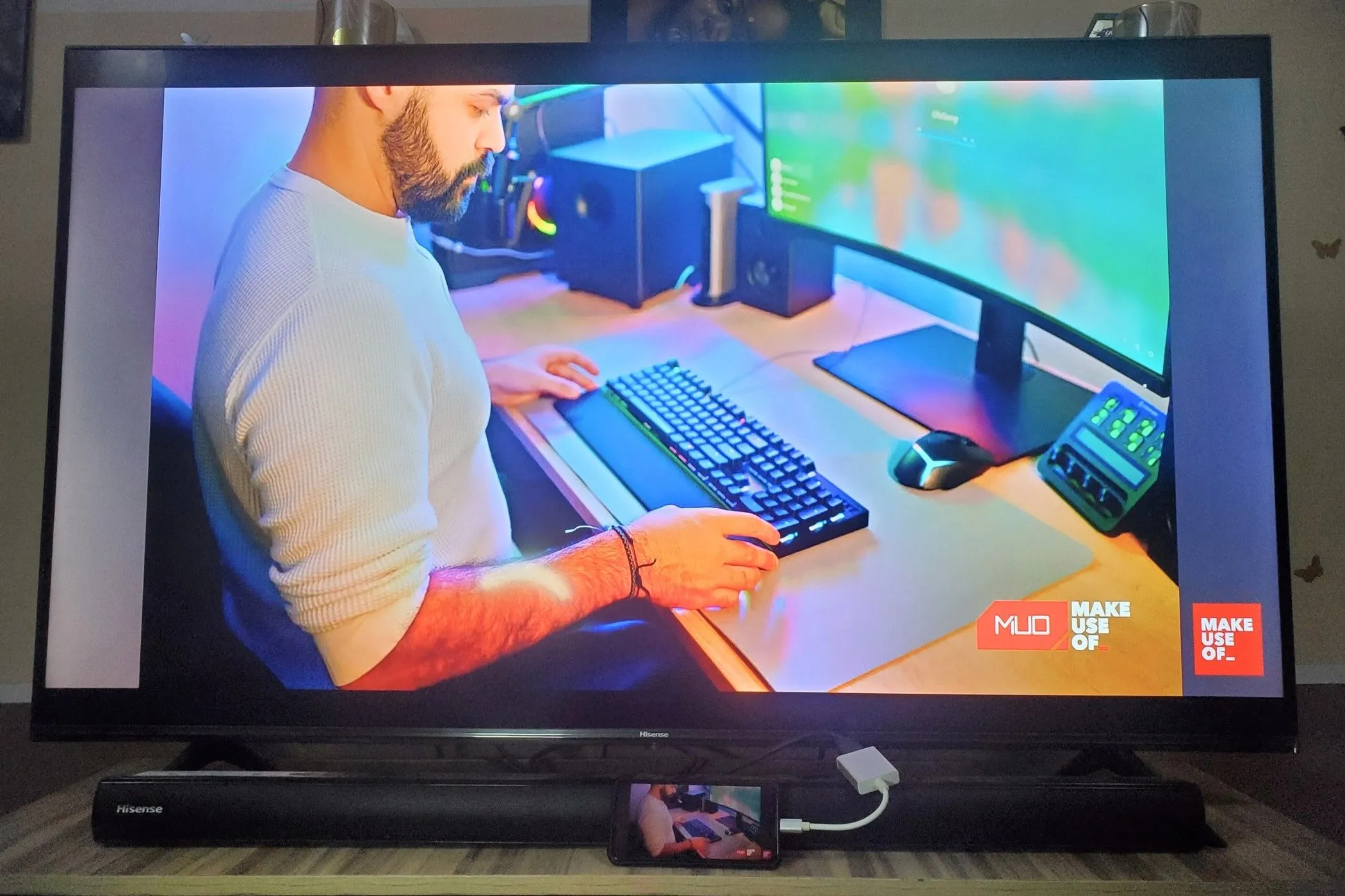 Một smartphone kết nối với TV qua adapter USB-C sang HDMI, đang chiếu màn hình và hiển thị một người đàn ông đang sử dụng bàn phím.