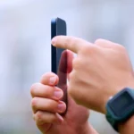 Người đàn ông tay phải cầm iPhone 15 Pro, ngón trỏ tay trái nhấn nút hành động ở cạnh bên