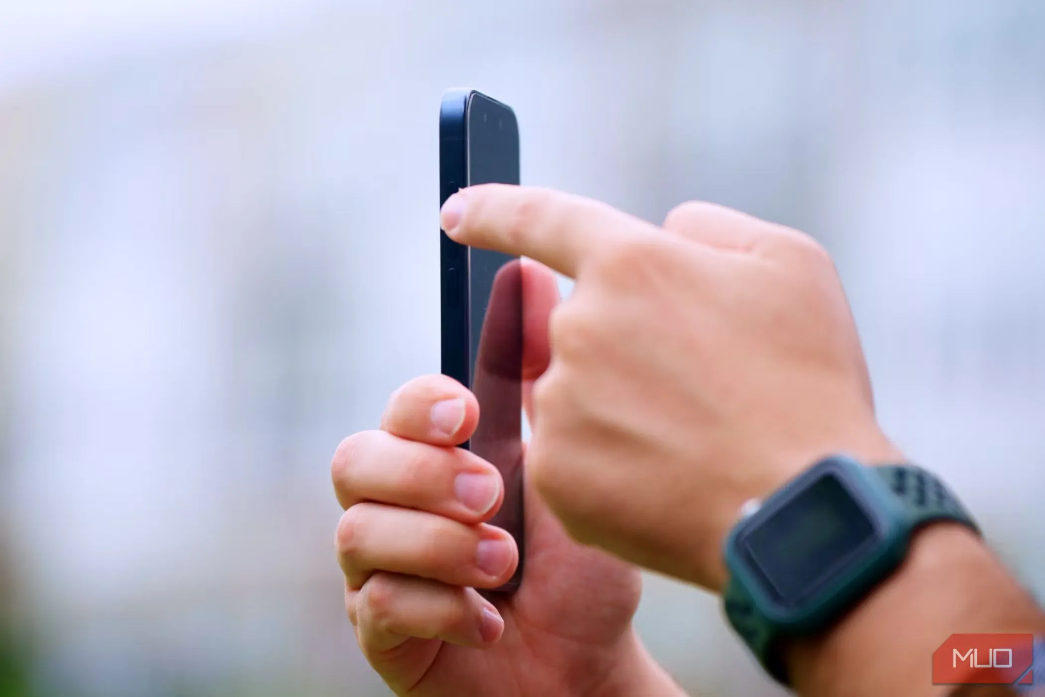 Người đàn ông tay phải cầm iPhone 15 Pro, ngón trỏ tay trái nhấn nút hành động ở cạnh bên