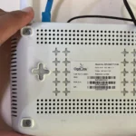 Người dùng cầm router và chỉ vào mặt sau, minh họa vị trí thông tin đăng nhập mặc định