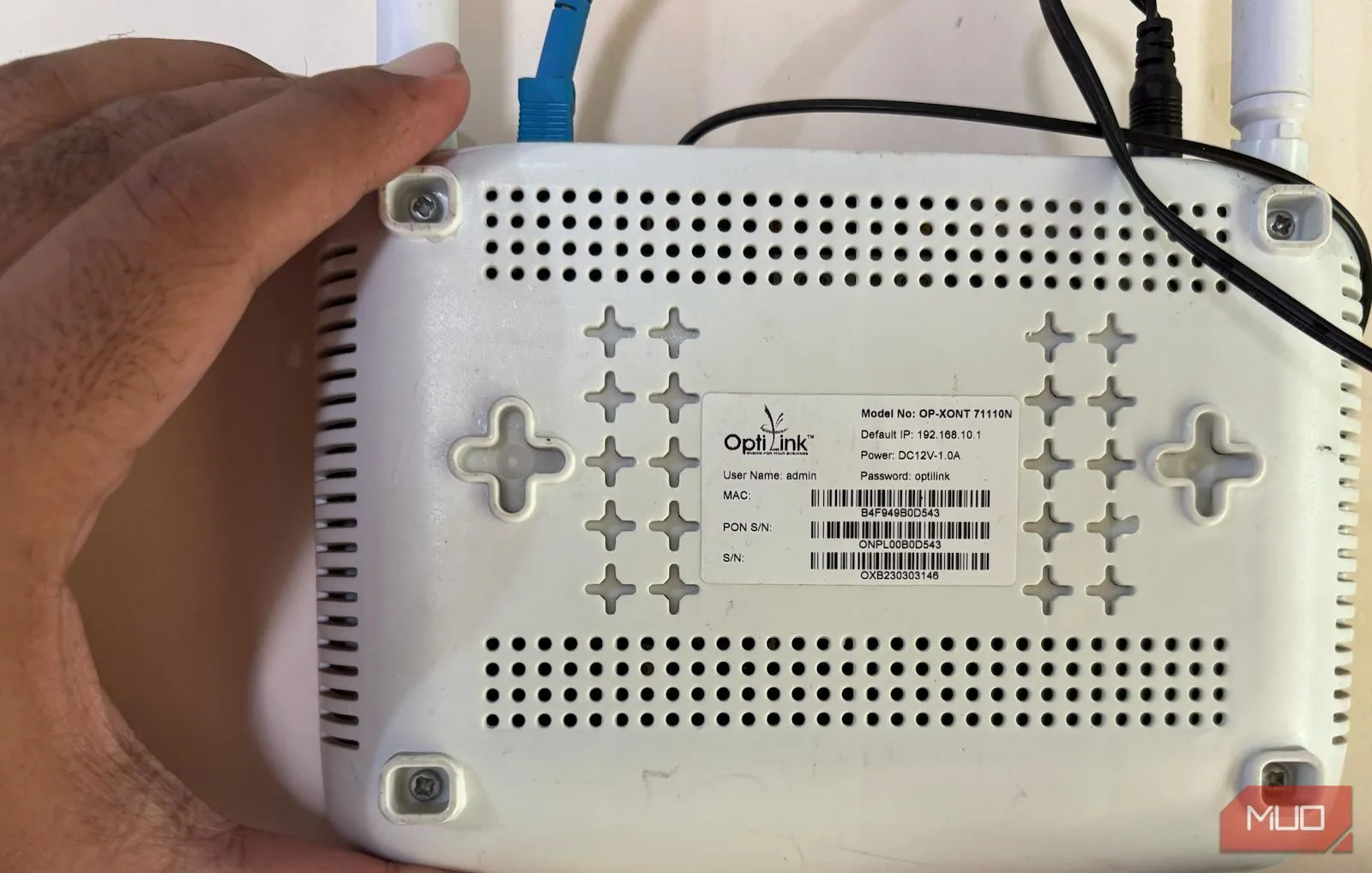 Người dùng cầm router và chỉ vào mặt sau, minh họa vị trí thông tin đăng nhập mặc định