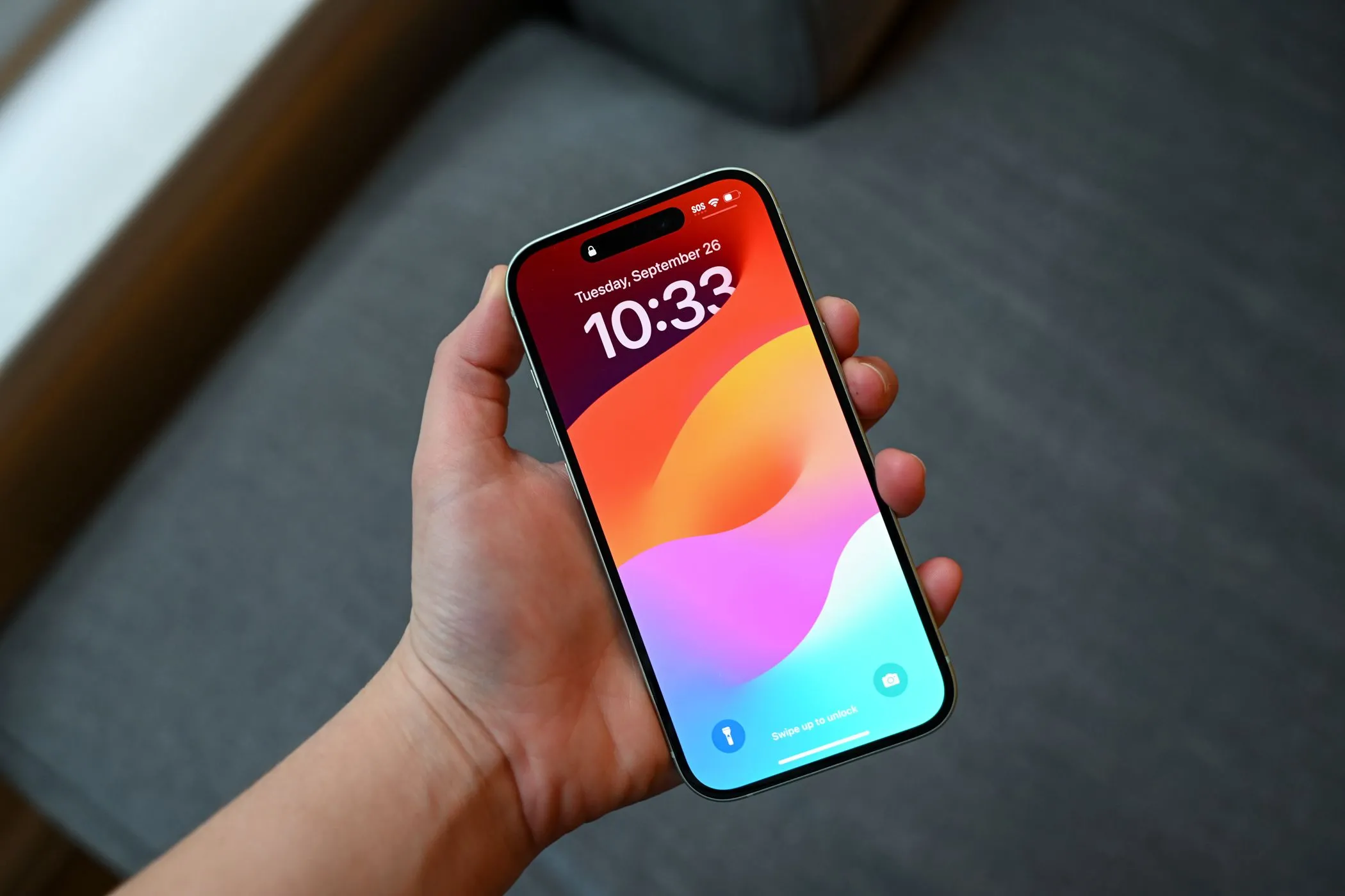 Người dùng đang cầm chiếc iPhone 15 hiển thị màn hình khóa, cho thấy tấm dán bảo mật có thể che đi các vết xước nhỏ trên màn hình cũ.