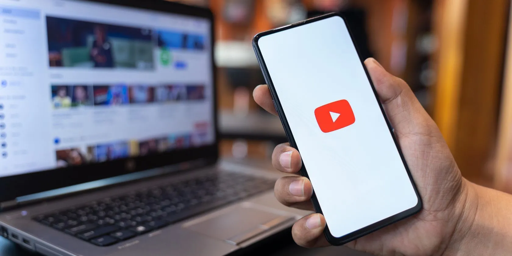 Người dùng đang cầm điện thoại với ứng dụng YouTube, biểu tượng YouTube ở nền sau