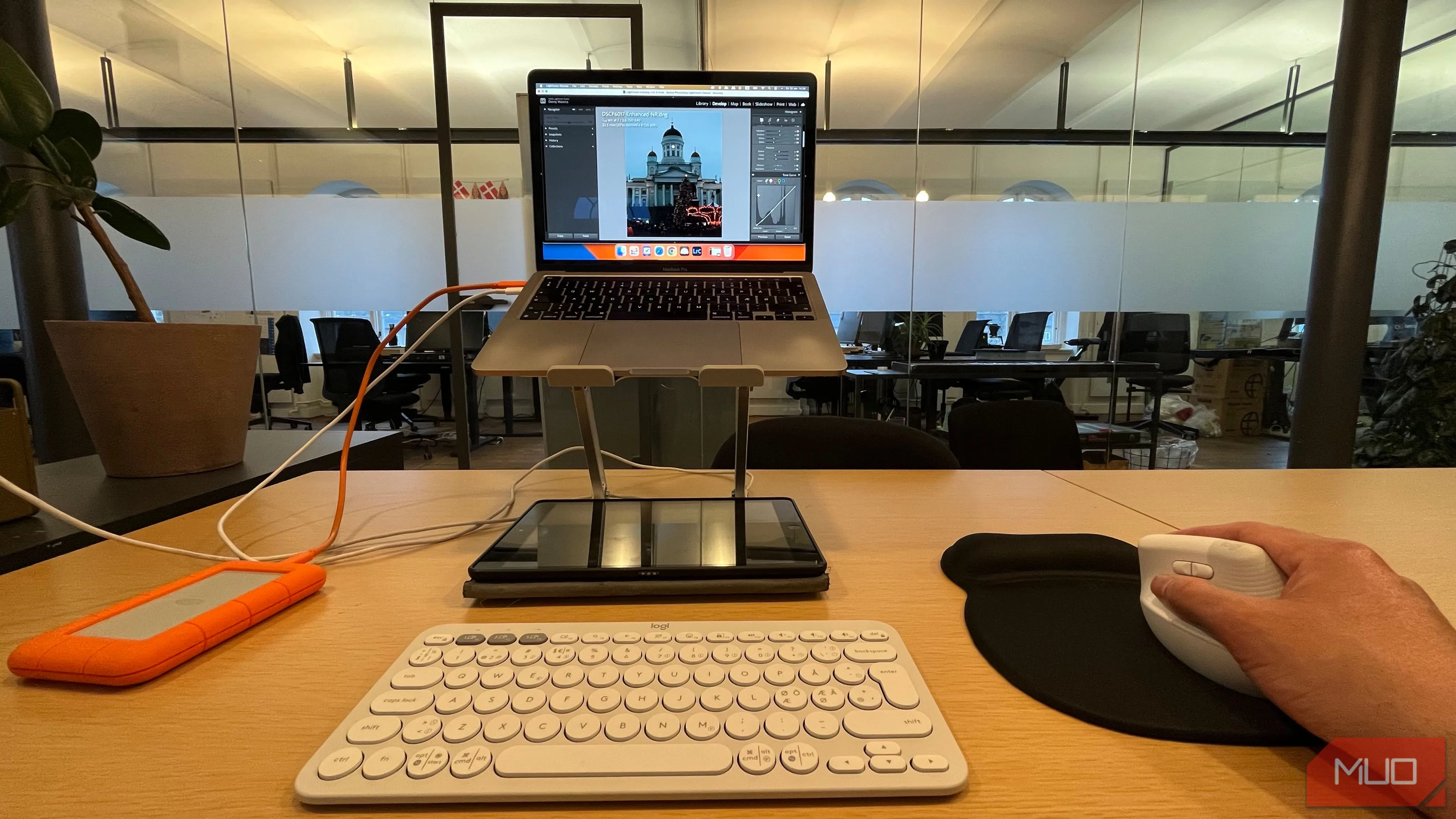 Người dùng đang chỉnh sửa ảnh trên laptop đặt trên đế nâng, sử dụng chuột không dây và bàn phím rời để làm việc hiệu quả