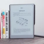 reMarkable Paper Pro đặt cạnh những cuốn sách trên bàn gỗ, thể hiện kích thước lớn hơn và vẻ ngoài cao cấp