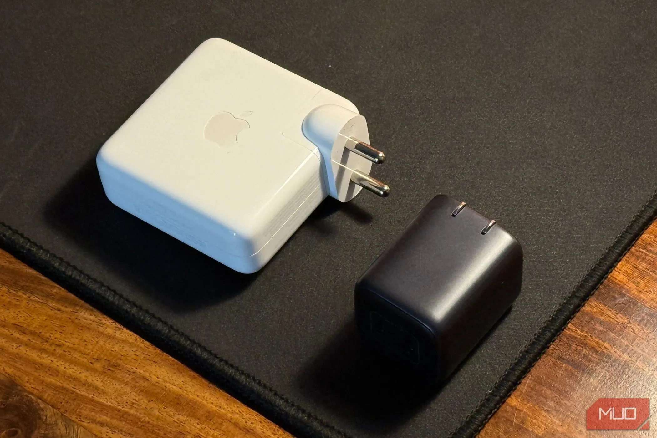 So sánh kích thước bộ sạc iPhone nhỏ gọn và bộ sạc MacBook lớn hơn, nhấn mạnh sự đa dạng phụ kiện Apple.