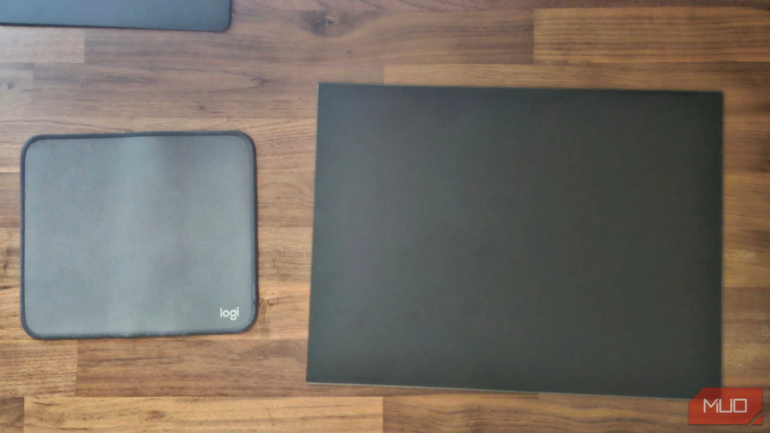 Thảm lót chuột Logitech và miếng lót chuột kính cường lực so sánh bên cạnh nhau, thể hiện sự khác biệt về chất liệu và thiết kế.