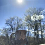 Cốc sứ trên lan can gỗ dưới nắng gắt, bầu trời xanh có HDR