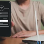 Người đàn ông cầm điện thoại cạnh bộ định tuyến, mô tả việc ẩn mạng Wi-Fi